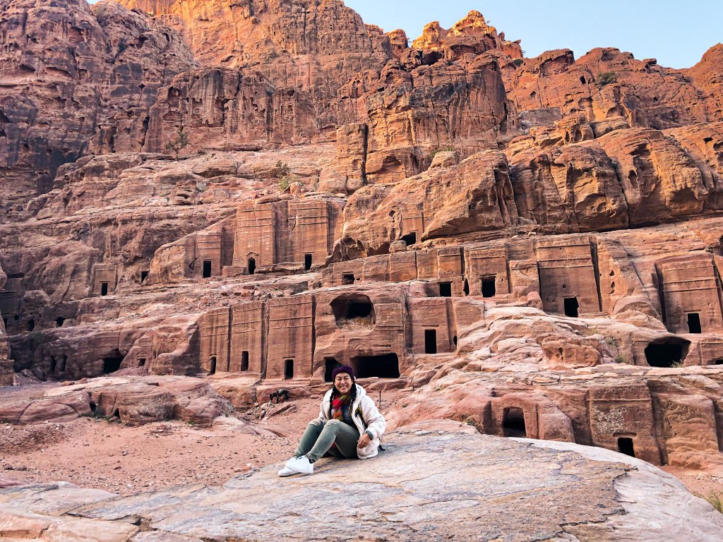 Me posing in front of many facades carved into the walls at Petra
